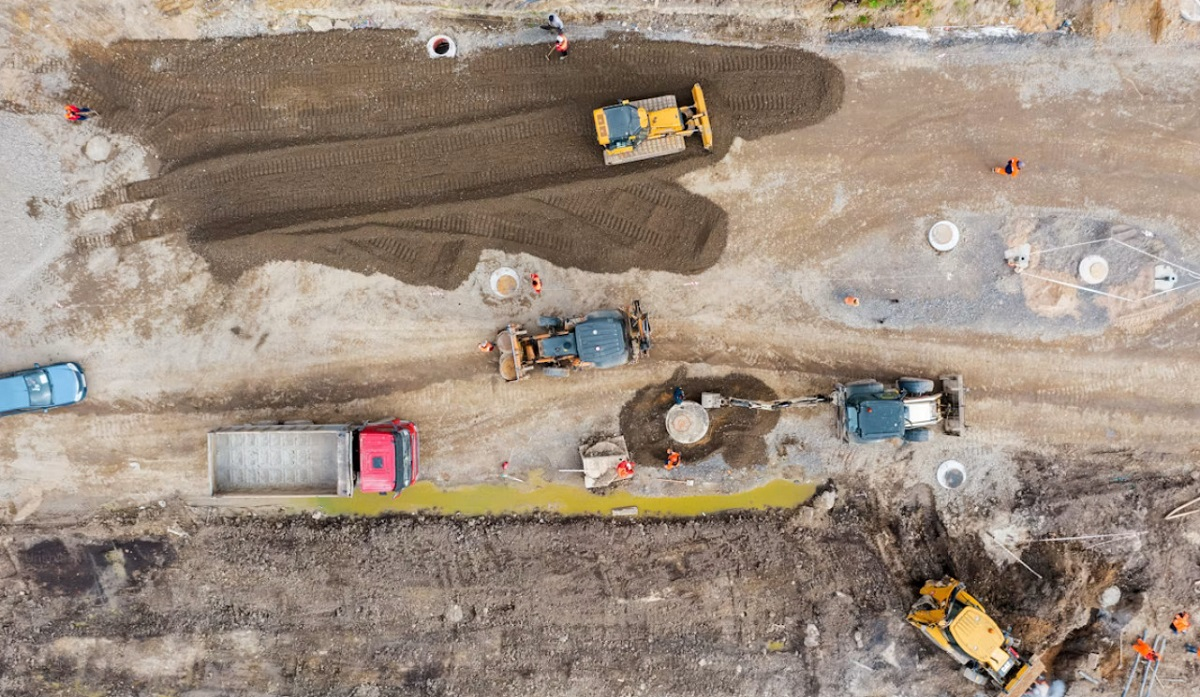 Pelleteuses et tractopelles préparant une tranchée sur un chantier de voirie avec des canalisations posées au sol.