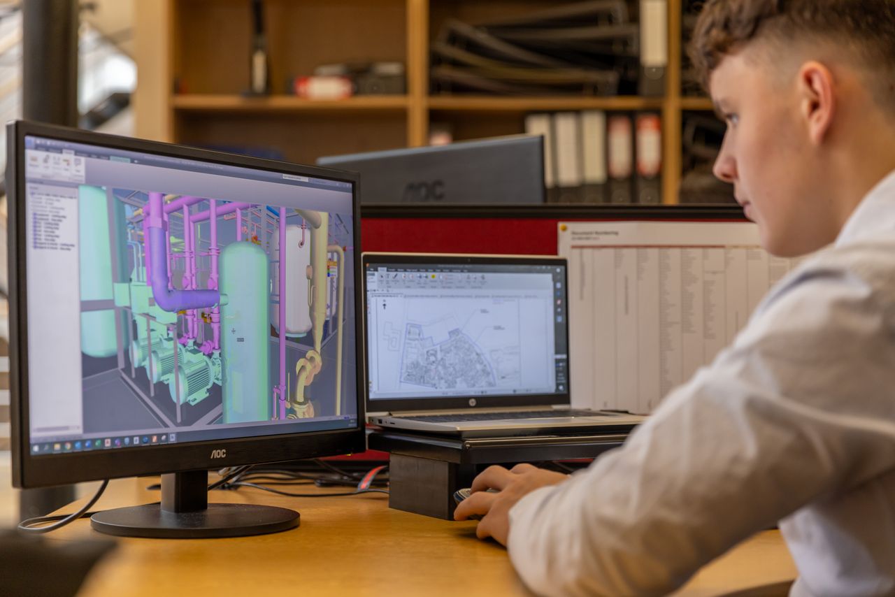 Maquette 3D d’un local technique avec tuyauteries, réservoirs et pompes, à côté d’un plan de masse 2D sur un portable